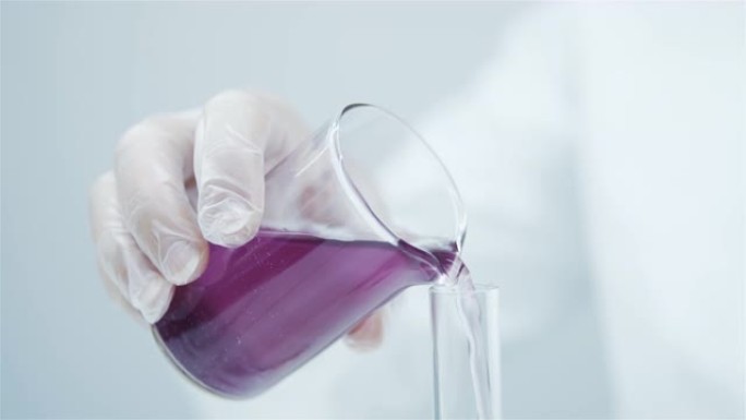 实验室助理的手放在白色医用手套上的特写镜头将粉红色的液体组合物倒入试管中。