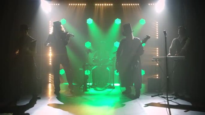 穿着老式爱尔兰服装和帽子的男性团体在绿色灯光的背景下在黑暗的工作室里唱歌和玩耍。音乐家演奏吉他、小提