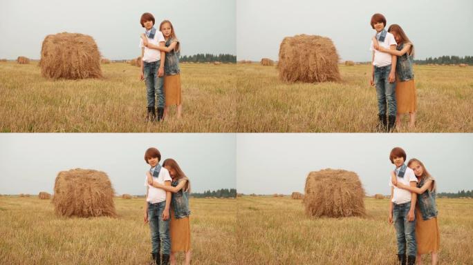 年轻夫妇在干草堆背景下拥抱收割地。拥抱十几岁的女孩和男孩在乡村草堆背景下摆姿势。