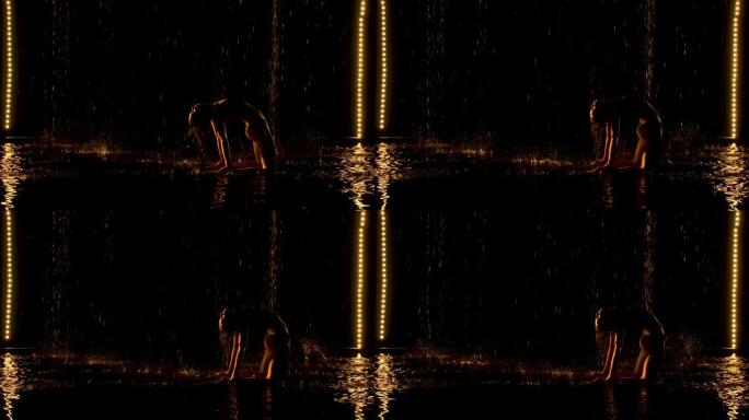 表演桥式姿势的迷人女人的剪影。黄光轻轻地落在一个年轻迷人女人的潮湿身体上。倾盆大雨的水上工作室。慢动