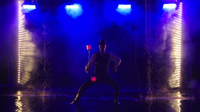 在一个黑烟的工作室里，一名男子被发光的红色手榴弹所映衬。一位时尚的艺人在背光蓝烟的背景下，在雨中表演