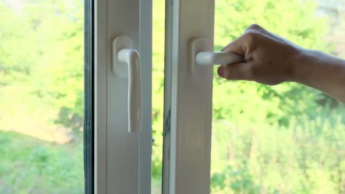 一名男子用把手关闭了一扇白色塑料窗。