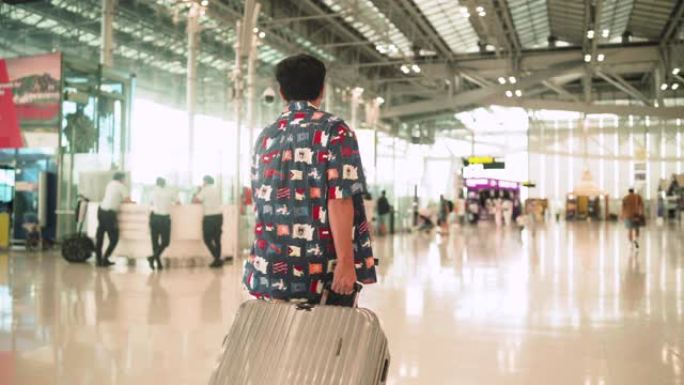 亚裔男子提着灰色行李箱，前往登机柜台航空公司机场
