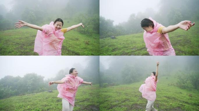 穿着粉红色雨衣的快乐年轻亚洲女性旅行者的慢动作享受和乐趣，在雨中与美丽的大自然一起旅行。微笑的漂亮女