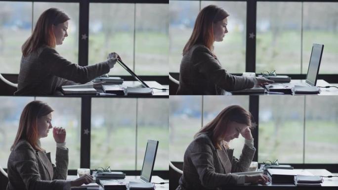 工作压力大，一个年轻疲惫的女商人因为网上工作问题而紧张，愤怒地敲桌子，关上笔记本电脑，坐在窗边的咖啡