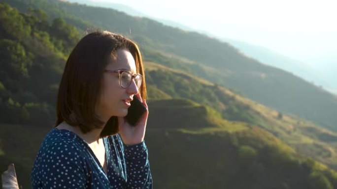 一位穿着礼服的年轻女子坐在山峦背景下在电话中讲话。这个女孩在高加索山区旅行。