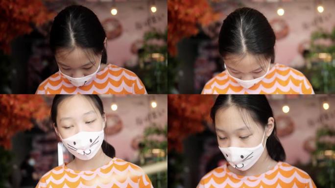 亚洲女孩戴着口罩，在餐厅等待她的食物订单与家庭，生活方式的概念。