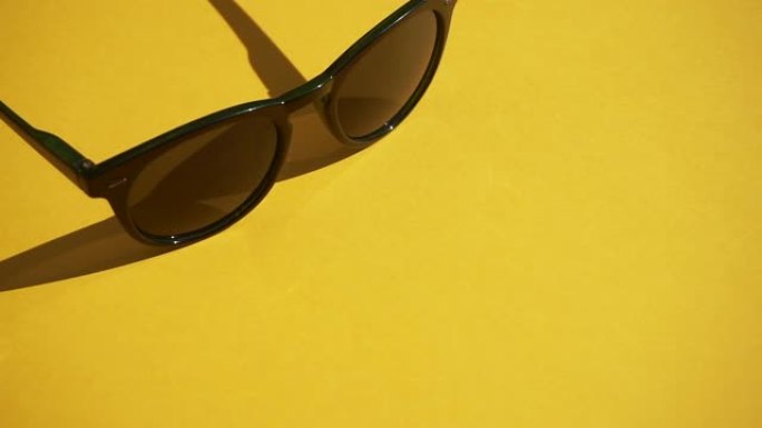 在白天的阳光下，黄色背景上的太阳镜。夏天，休息和放松的概念。最小平面视频