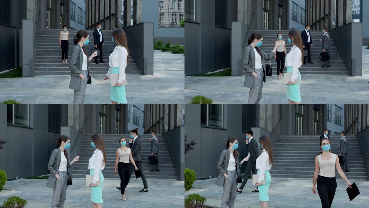 两个戴着防护面具的女商人站在办公楼外讨论。自信的女人向女同事解释某些事情
