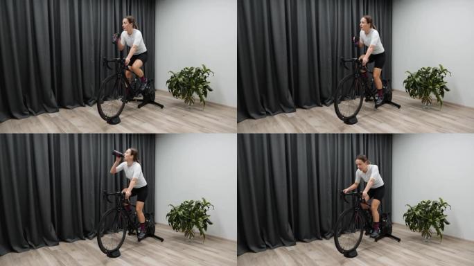 骑自行车的室内智能教练的女人在骑自行车时喝水或等渗饮料。专业自行车训练计划