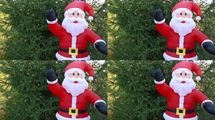 穿着红色西装的真人大小的充气圣诞老人娃娃站在绿树的背景下。新年快乐庆祝，节日快乐