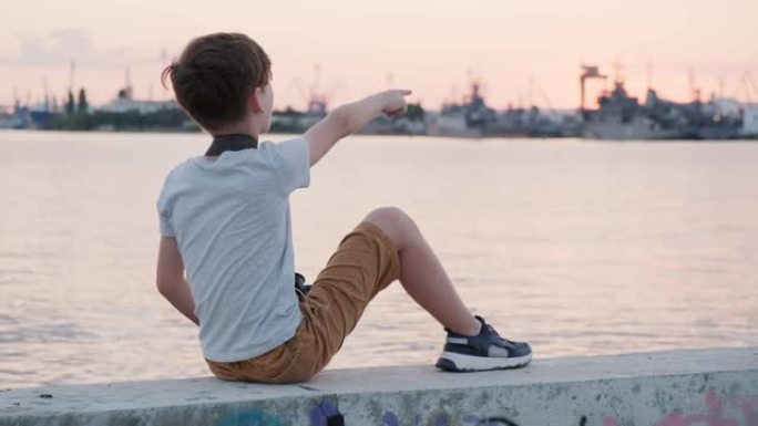 快乐男孩拿着双筒望远镜，在明亮的日落时向远处望去，用手在海港码头的阳光下展示。安静的水域。儿童暑假。