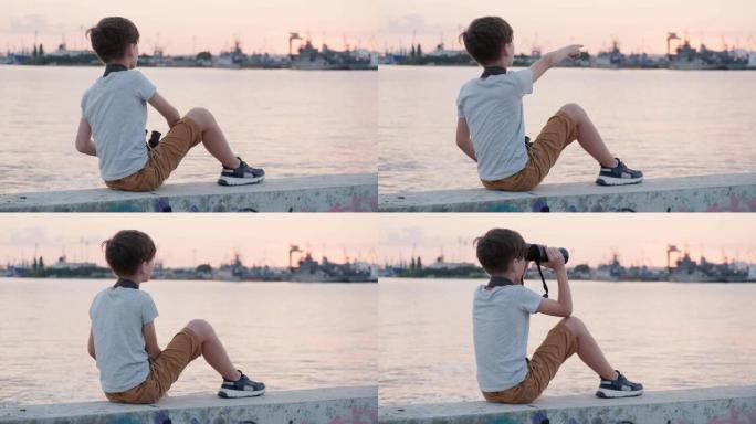快乐男孩拿着双筒望远镜，在明亮的日落时向远处望去，用手在海港码头的阳光下展示。安静的水域。儿童暑假。