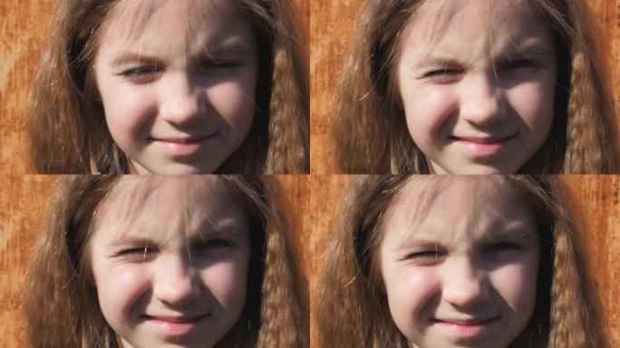 美丽的小孩的肖像，金发斜视着，看着户外的相机。特写微笑的小女孩的快乐女性脸，被阳光照亮，外面有积极的