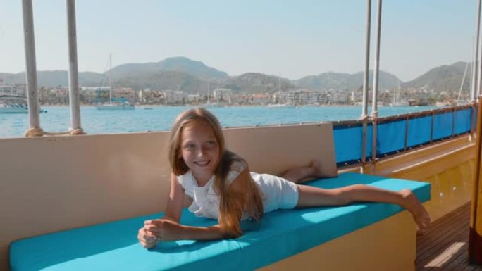 无忧无虑的女孩在沙发帆船上放松，海上巡游在山景上。夏季旅行时，旅游女孩躺在海上沙发上散步。