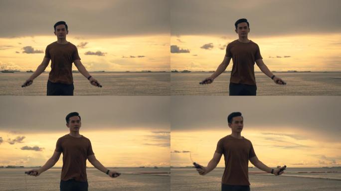一个英俊的亚洲运动员穿着运动服跳绳，在夏天美丽的日落时在海滩上锻炼。