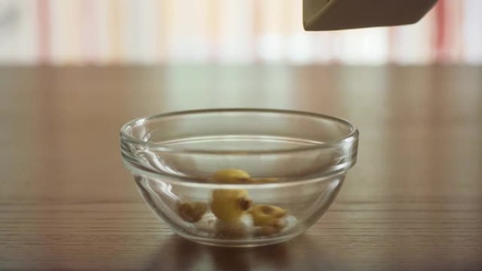 将脆饼和玉米片放入透明的玻璃碗中，以便早晨在家在阳光下的木制桌子上做饭。