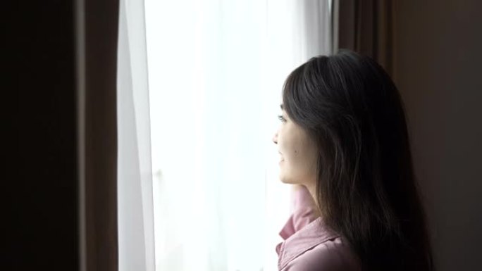 亚洲年轻女子清晨透过窗户看风景的慢动作场景 (4K)