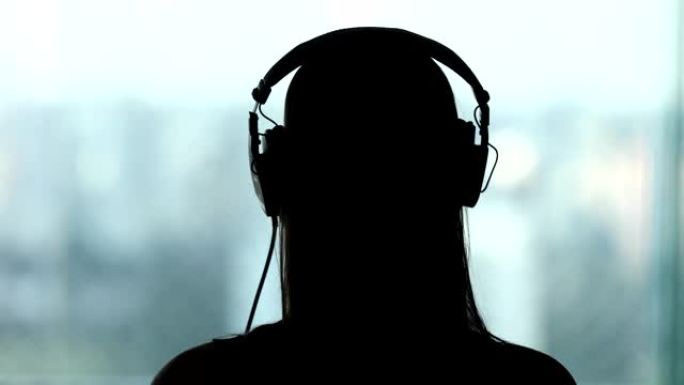 戴上耳机的女人的背部，听音乐，歌曲，播客或有声读物的人的剪影
