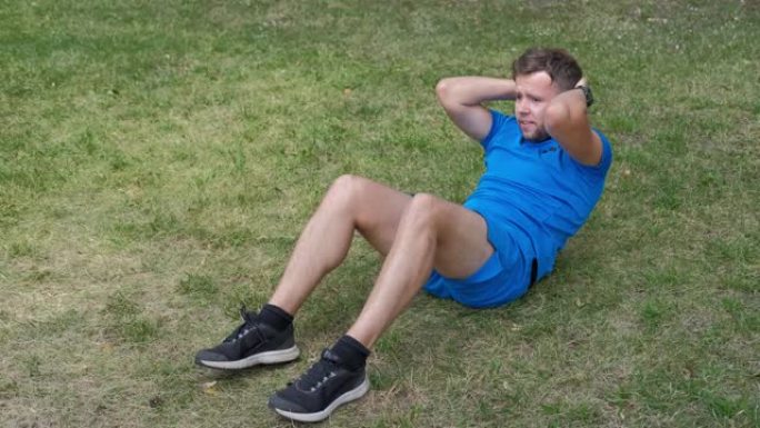 男子在训练期间在公园的草地上摇晃腹部肌肉。