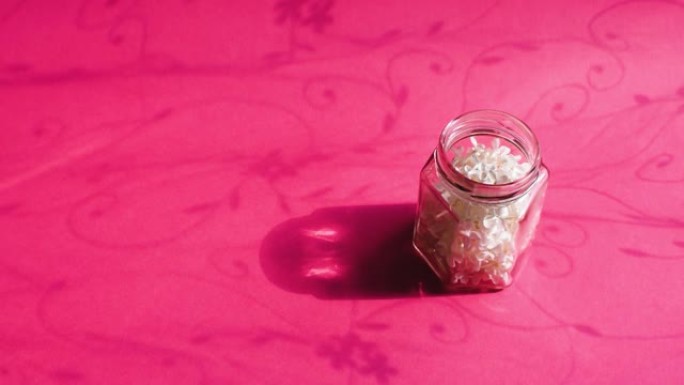 白色的鸟樱桃树花在粉红色背景上的透明玻璃罐中