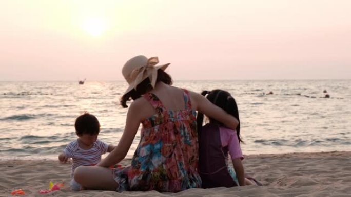 亚洲幸福家庭晚上在沙滩上玩沙子，背景是大海。母亲照顾她的孩子坐在孩子旁边。婴儿和妹妹感觉享受有趣的活