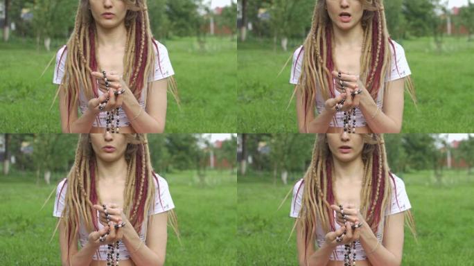 年轻漂亮的长辫子女孩手里拿着天然石头做的项链，早上在后院的绿草上冥想
