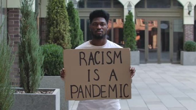 一名年轻的非洲裔美国人站在纸板海报上，种族主义是公共户外场所的一种流行病。街头示威。慢动作。特写