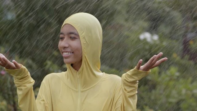 快乐的亚洲女孩在雨中玩耍，在大自然中享受乐趣。慢动作