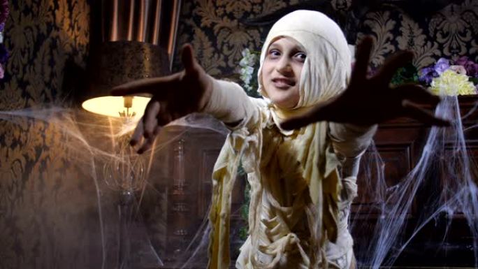 穿着万圣节木乃伊服装的女孩在古老的黑暗哥特式室内布满蜘蛛网和神秘雾的背景下摆姿势和吓人的电影镜头。4