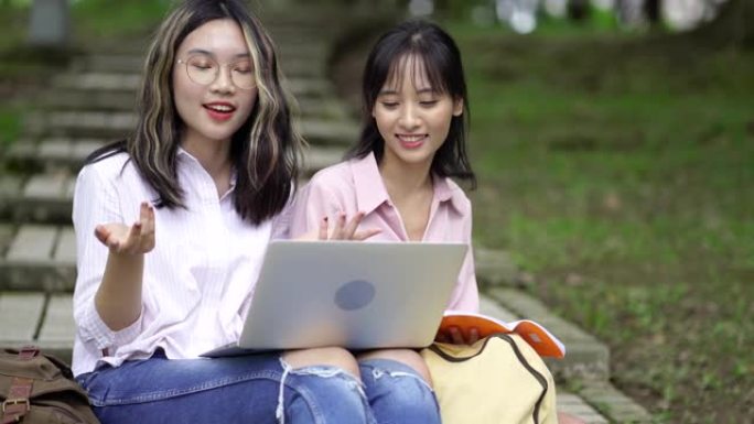 两名年轻的亚洲女学生在公园使用笔记本电脑