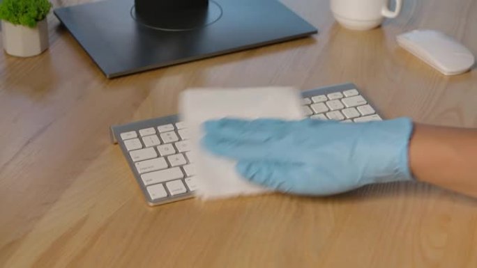 双手戴着保护性乳胶手套，在键盘表面喷洒防腐剂，并用餐巾纸彻底清除危险的病毒，细菌和细菌。特写。慢动作