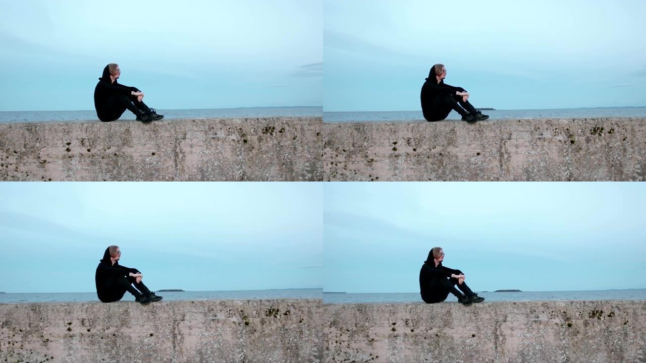 一个穿着黑色衣服的年轻人的肖像，他坐在海边的码头上放松