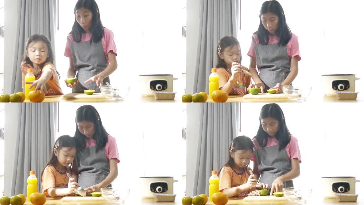 亚洲女孩教她的妹妹如何挤橙汁在家里加工甜果冻。