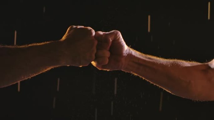 在雨中黑色背景上，男运动员的两个拳头的冲突。慢动作。特写