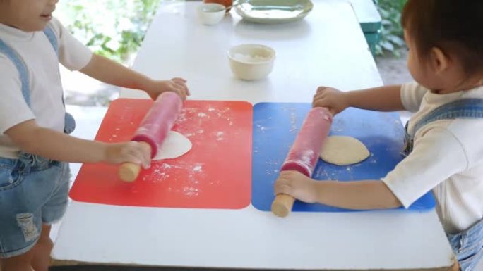 快乐的孩子在厨房为自制比萨饼准备面团，用rolling面杖和面粉在桌子上铺开面团。家庭乐趣和烹饪概念