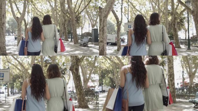 两名妇女带着购物袋走在街上的后视图