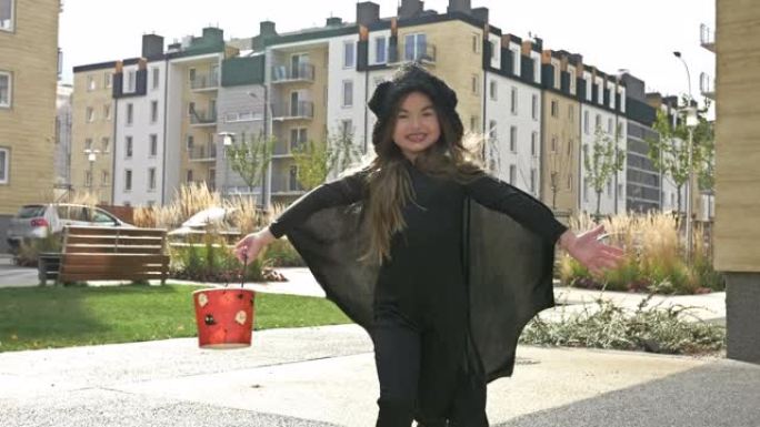 万圣节。一个穿着蝙蝠化装的6-7岁女孩带着水桶快乐地跑到街上收集糖果