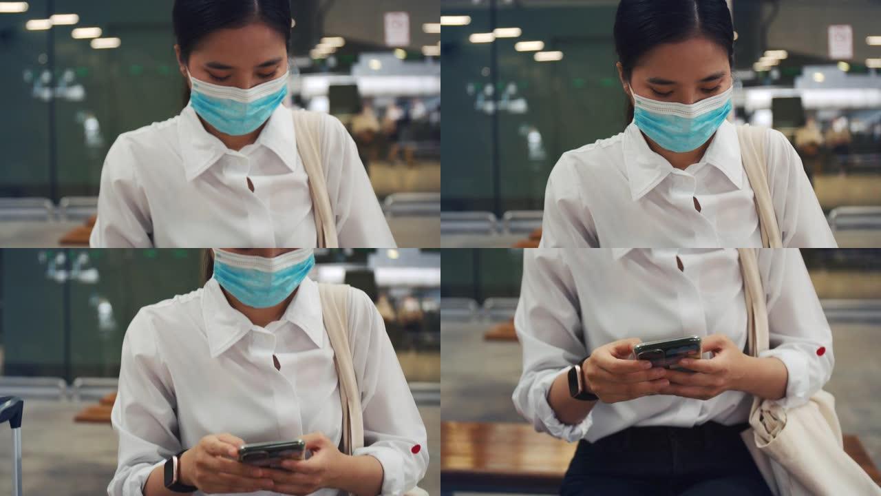 年轻女性戴着外科口罩保护，在机场航站楼使用智能手机，并在新型冠状病毒肺炎大流行期间保持社交距离。