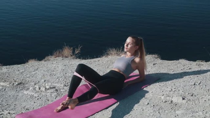 女孩躺在垫子上，用橡皮筋锻炼身体，训练臀部，身体
