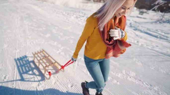 微笑的女人拉着雪橇上坡，准备在雪山上乘新的雪橇