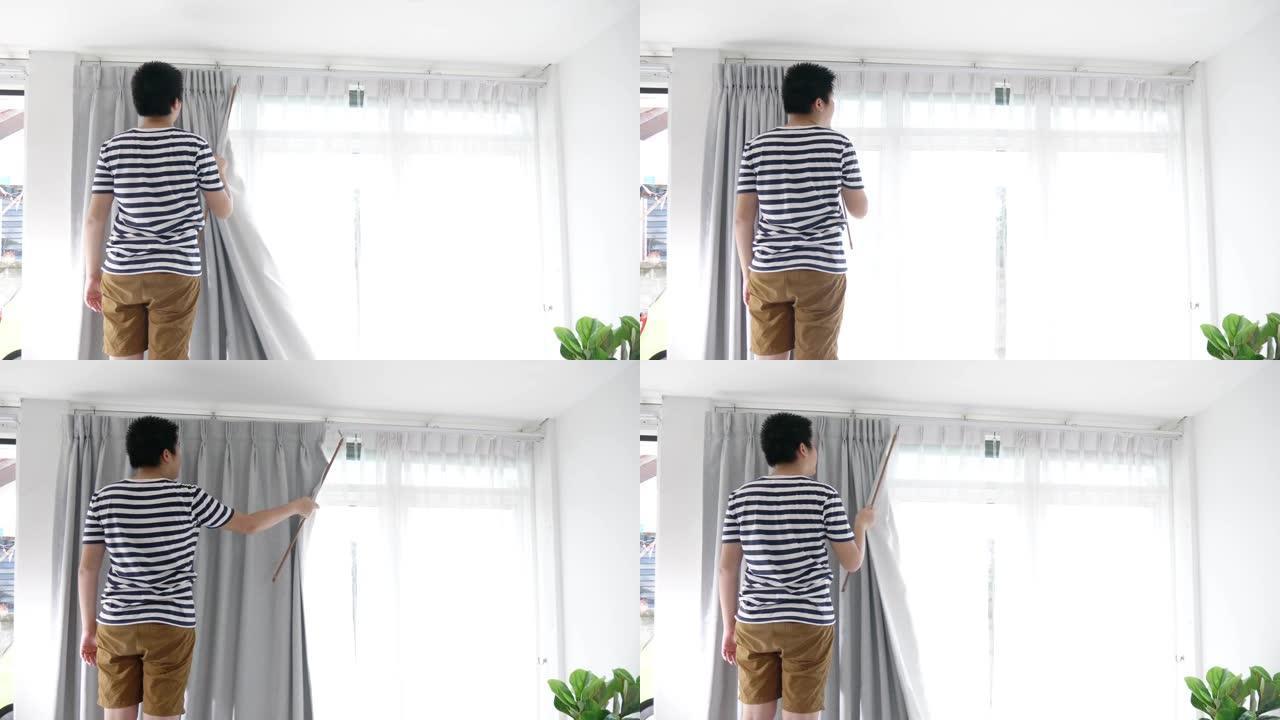 亚洲男孩haning窗帘与窗户在家里，搬家的概念。