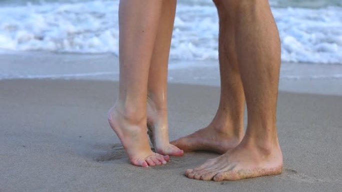 年轻恋人的脚在海浪中亲吻