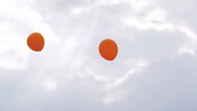 在户外节日上，橙色气球在风中摇曳，在灰色的天空中摇摆