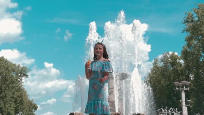 喷泉附近一个穿着全长连衣裙的漂亮女孩吹泡泡。