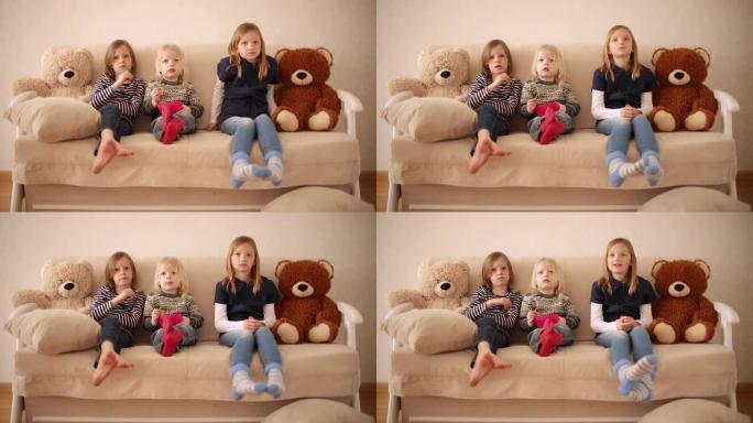 有趣的小男孩 (3岁) 和姐姐 (8岁和9岁) 一起看动画片。兄弟姐妹坐在沙发上吃饼干