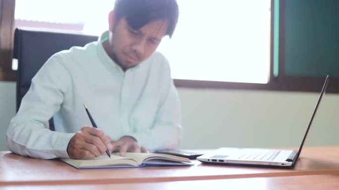 年轻的亚洲商人在办公室的木桌背景上做笔记本和笔记本电脑的商业计划书