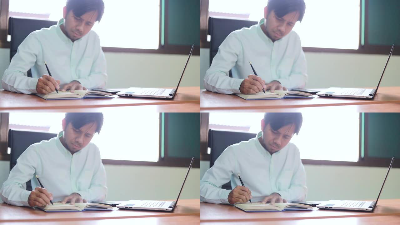 年轻的亚洲商人在办公室的木桌背景上做笔记本和笔记本电脑的商业计划书