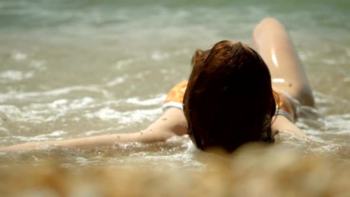 穿着泳衣躺在沙滩上的美丽幸福女人。地中海沿岸的海浪破裂。希腊。慢动作。高清