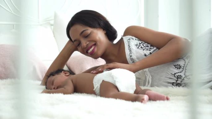 前视图: 一位非洲母亲的肖像，早晨有一个非洲新生婴儿睡在白色床上，年轻女子使三个月大的可爱的小男孩平